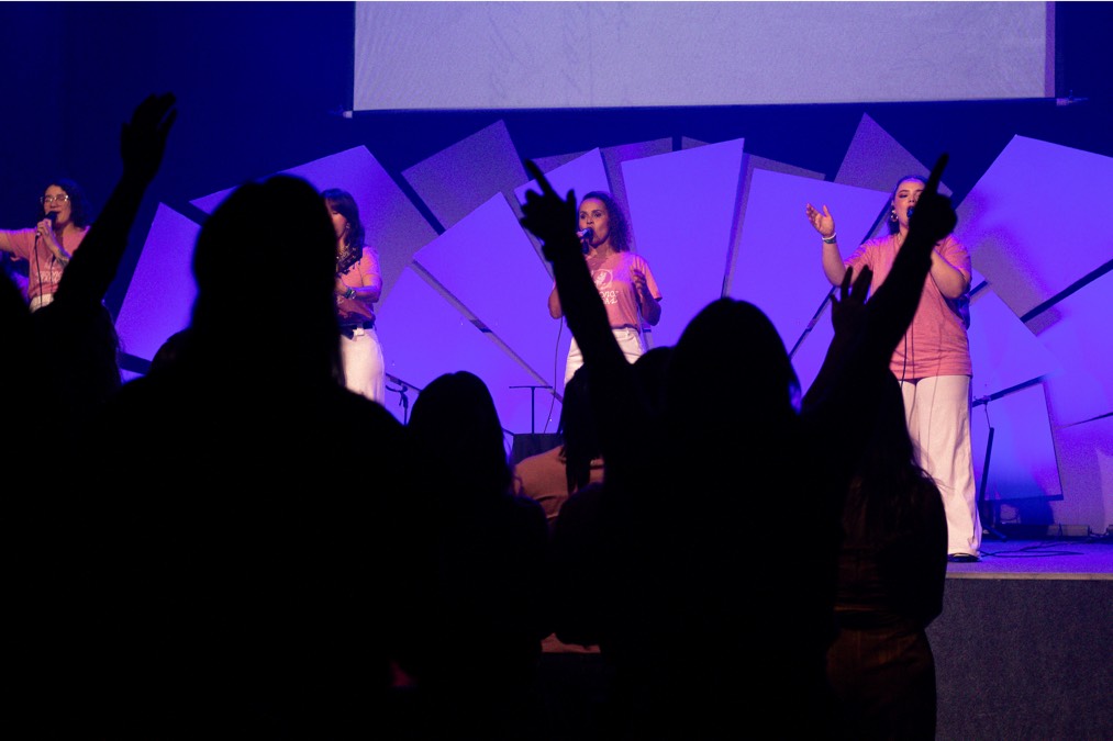 Back of a man at a concert. Hes wearing a beanie hat and a baggy denim jacket with studs. Photo with a purple hue